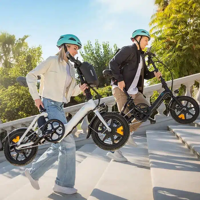 Ein Mann und eine Frau tragen jeweils ein weißes und ein schwarzes Fiido D3 Pro Mini E-Bike auf einer Steintreppe in der Sonne.