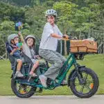 Eine Frau fährt ein grünes Fiido T2 Lastenrad mit zwei Kindern auf Kindersitzen im Park.
