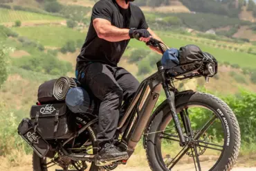 Mann in schwarzer Kleidung und Helm fährt ein schwer beladenes schwarzes Fiido Titan E-Bike mit breiten Fat-Reifen auf einem Feldweg.