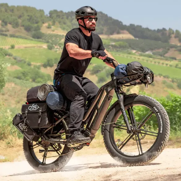 Mann in schwarzer Kleidung und Helm fährt ein schwer beladenes schwarzes Fiido Titan E-Bike mit breiten Fat-Reifen auf einem Feldweg.