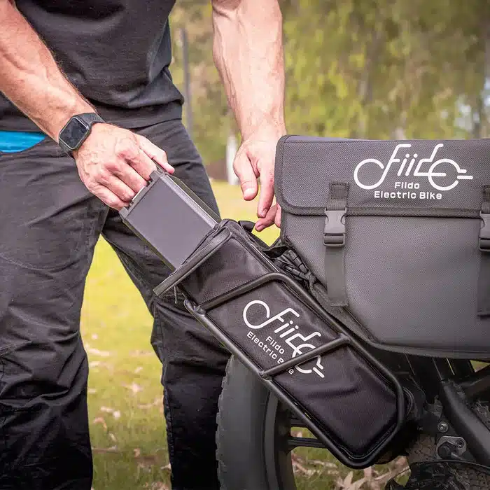Mann entnimmt einen Akku aus einer Tasche am Heckgepäckträger eines Fiido Titan E-Bikes.