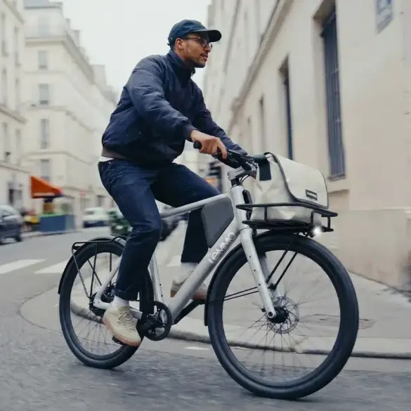Ein Mann fährt ein Lemmo One Collab. Ride Fahrrad mit Gepäckträger und Tasche auf einer Straße.