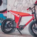 Rotes MOTO E-Bike mit breiten Reifen und auffälligem Design, abgestellt vor einer Graffiti-Wand und einer Steinfassade.