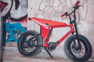 Rotes MOTO E-Bike mit breiten Reifen und auffälligem Design, abgestellt vor einer Graffiti-Wand und einer Steinfassade.