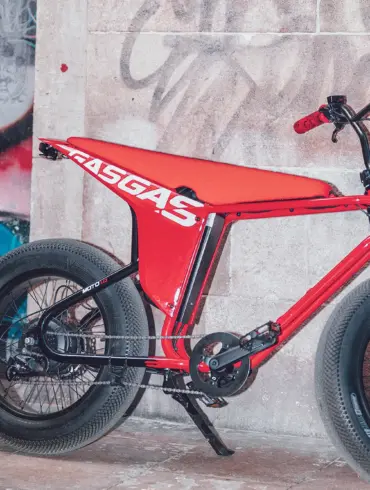 Rotes MOTO E-Bike mit breiten Reifen und auffälligem Design, abgestellt vor einer Graffiti-Wand und einer Steinfassade.