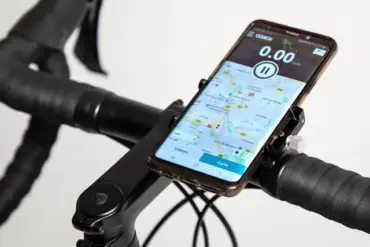Detailansicht einer schwarzen Metall-Smartphonehalterung, befestigt an einem Fahrradlenker. Ein Smartphone mit Karten-App und Tachometer ist in der Halterung angebracht.