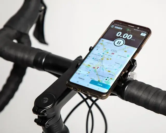 Detailansicht einer schwarzen Metall-Smartphonehalterung, befestigt an einem Fahrradlenker. Ein Smartphone mit Karten-App und Tachometer ist in der Halterung angebracht.
