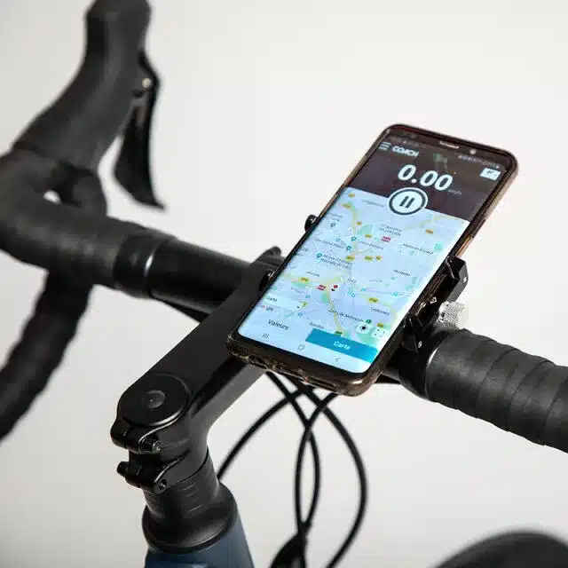 Detailansicht einer schwarzen Metall-Smartphonehalterung, befestigt an einem Fahrradlenker. Ein Smartphone mit Karten-App und Tachometer ist in der Halterung angebracht.