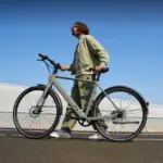 Ein Mann in legerer Kleidung schiebt ein graues TENWAYS CGO600 Pro E-Bike im Freien.