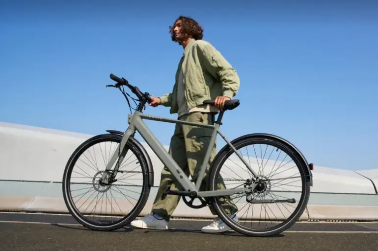 Ein Mann in legerer Kleidung schiebt ein graues TENWAYS CGO600 Pro E-Bike im Freien.