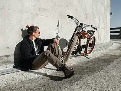 Mann sitzt lässig neben einem roten und beigen E-Bike.