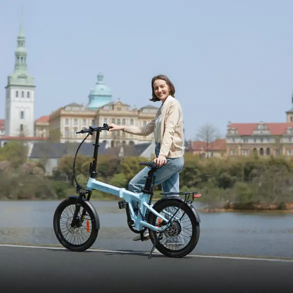Frau auf einem hellblauen ADO Air 20 Pro Elektro-Faltrad neben einem See, mit historischer Stadtarchitektur im Hintergrund.