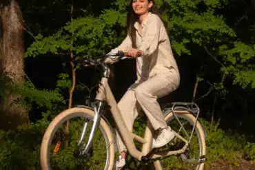 Eine lächelnde Frau sitzt auf einem beigen ADO Air 28 Pro E-Bike und fährt auf einem Weg im Freien.
