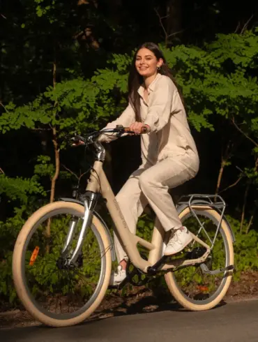 Eine lächelnde Frau sitzt auf einem beigen ADO Air 28 Pro E-Bike und fährt auf einem Weg im Freien.