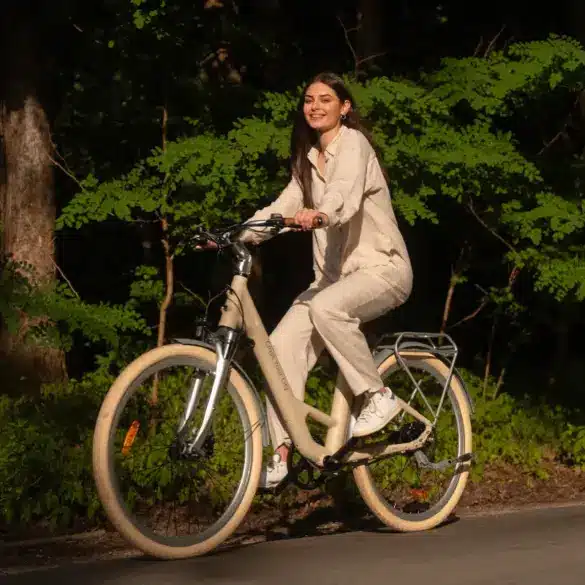 Eine lächelnde Frau sitzt auf einem beigen ADO Air 28 Pro E-Bike und fährt auf einem Weg im Freien.