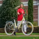 Frau mit einem cremefarbenen ADO Air 28 City-E-Bike im Freien, mit Fokus auf das Fahrrad und seinen tiefen Einstieg.
