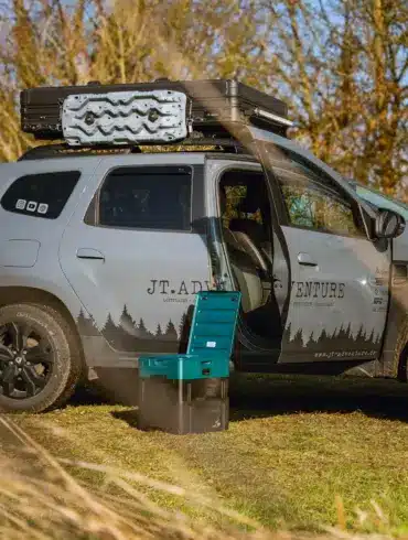 Portable Verschweißtoilette vor einem mit Dachgepäck und Dachzelt ausgestatteten Dacia Duster