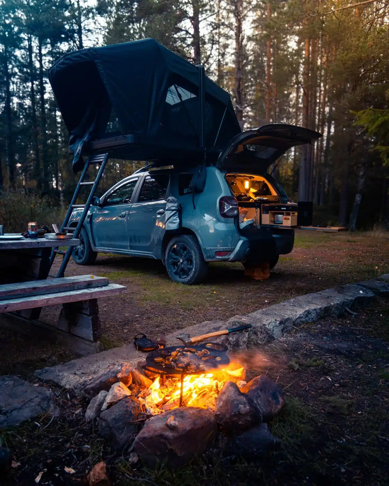 Dacia Duster mit aufgebautem Dachzelt und geöffneter Heckklappe auf einem Waldcampingplatz