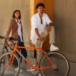 Mann und Frau neben einem orangefarbenen Rennrad, das an ein historisches Modell erinnert.