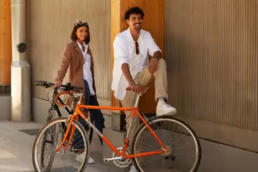 Mann und Frau neben einem orangefarbenen Rennrad, das an ein historisches Modell erinnert.