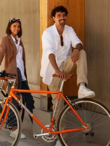 Mann und Frau neben einem orangefarbenen Rennrad, das an ein historisches Modell erinnert.