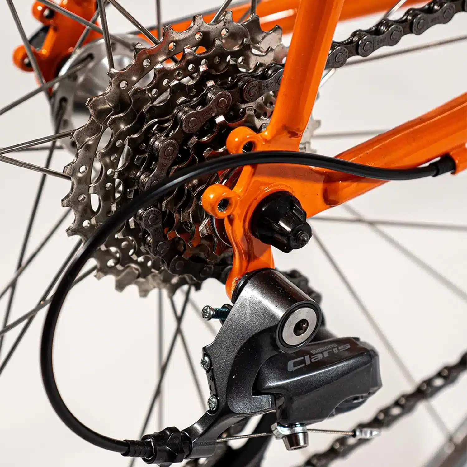 Nahaufnahme des orangefarbenen Fahrradrahmens mit dem Shimano Claris Schaltwerk, der Fahrradkette und der Kassette