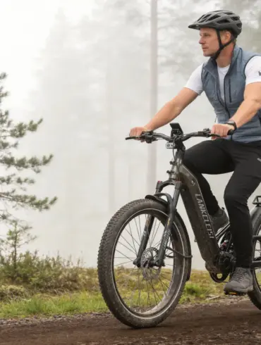 Ein Mann mit Helm fährt ein LANKELEISI KETT-8 E-Bike mit breiten Reifen und vollgefedertem Rahmen auf einem Feldweg in einer nebligen Waldlandschaft.
