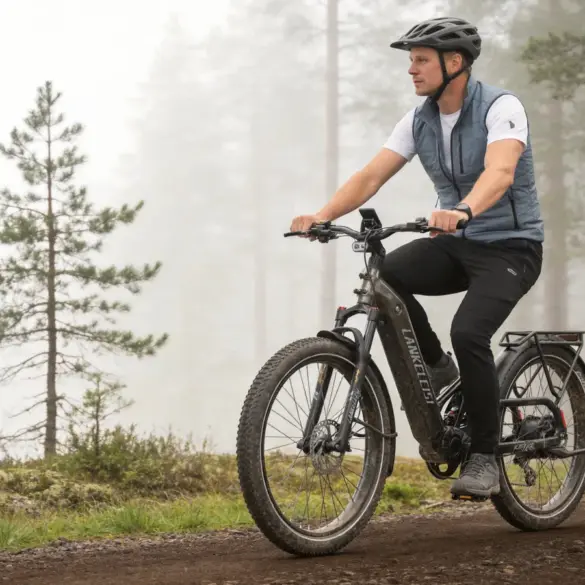 Ein Mann mit Helm fährt ein LANKELEISI KETT-8 E-Bike mit breiten Reifen und vollgefedertem Rahmen auf einem Feldweg in einer nebligen Waldlandschaft.
