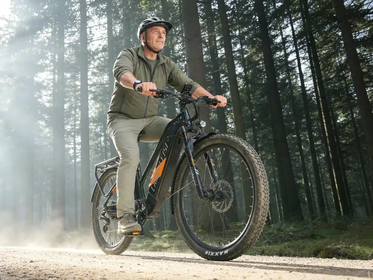Mann fährt LANKELEISI MX600PRO E-Bike auf einem staubigen Waldweg im Wald.