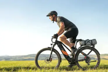 Ein Mann in Radlerkleidung und Helm fährt ein schwarzes Trekking-E-Bike auf einem Feldweg bei strahlendem Sonnenschein.