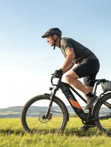 Ein Mann in Radlerkleidung und Helm fährt ein schwarzes Trekking-E-Bike auf einem Feldweg bei strahlendem Sonnenschein.
