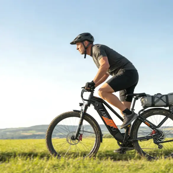 Ein Mann in Radlerkleidung und Helm fährt ein schwarzes Trekking-E-Bike auf einem Feldweg bei strahlendem Sonnenschein.