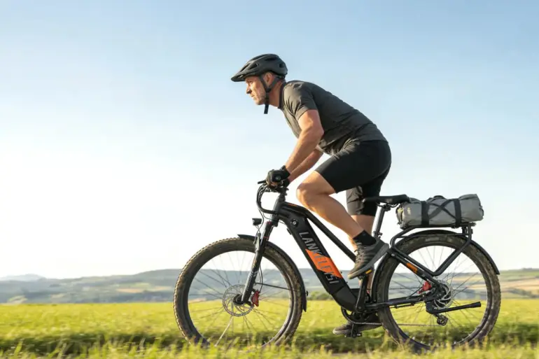 Ein Mann in Radlerkleidung und Helm fährt ein schwarzes Trekking-E-Bike auf einem Feldweg bei strahlendem Sonnenschein.