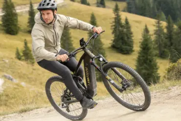 Ein Mann fährt ein schwarzes E-Mountainbike mit dem Namen LANKELEISI auf einem Schotterweg in den Bergen.