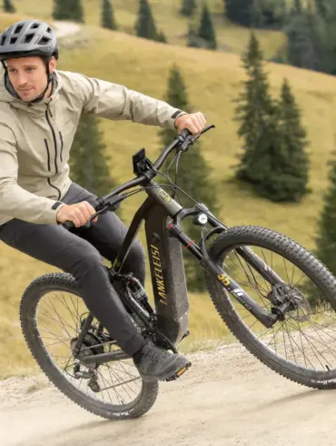 Ein Mann fährt ein schwarzes E-Mountainbike mit dem Namen LANKELEISI auf einem Schotterweg in den Bergen.