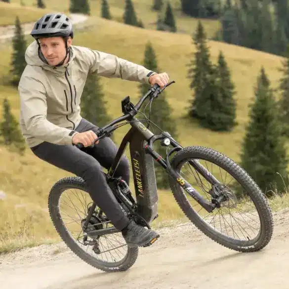 Ein Mann fährt ein schwarzes E-Mountainbike mit dem Namen LANKELEISI auf einem Schotterweg in den Bergen.