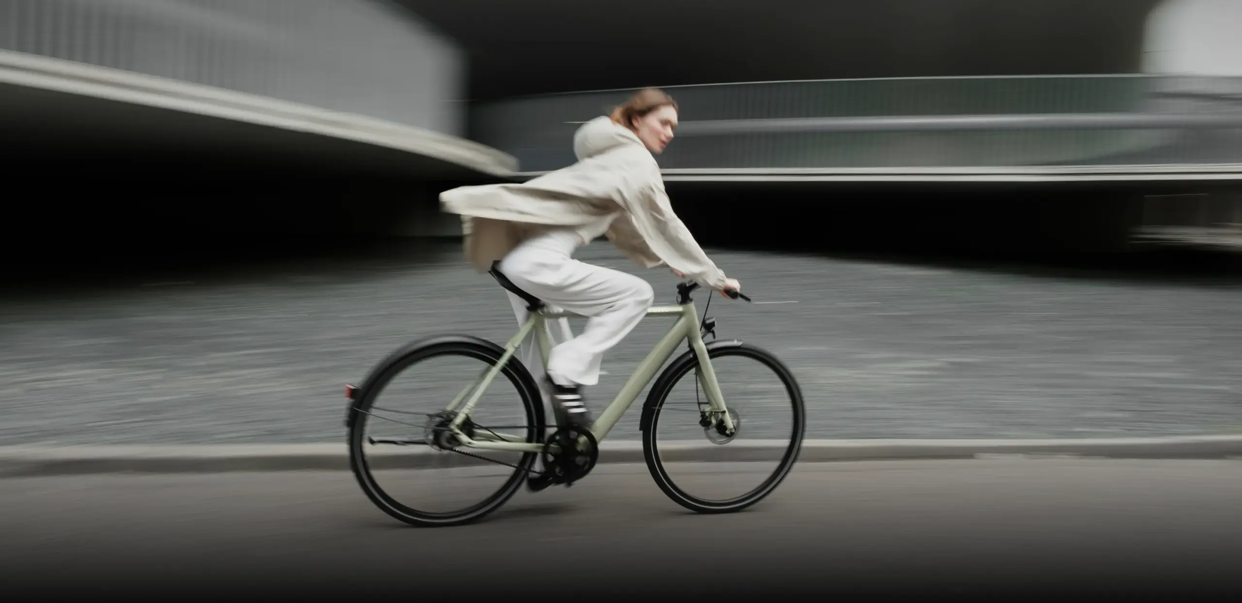 Eine Person fährt ein hellgrünes TENWAYS CGO600 E-Bike auf einer asphaltierten Straße in der Stadt, mit einem Hintergrund aus Betonstrukturen.