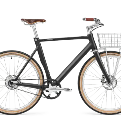 Schwarz mattes Arthur Cruiser E-Bike mit braunem Ledersattel, braunen Griffen und einem silbernen Frontkorb, ausgestattet mit Schutzblechen und einem Zahnriemenantrieb.