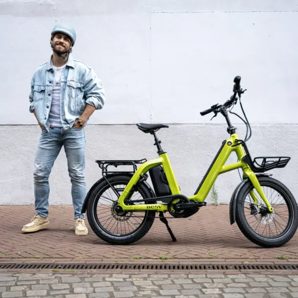 Limegrünes BESV CPT 1.0 E-Bike mit vorne montiertem Gepäckträger und hinterem Gepäckträger, daneben ein Mann mit Jeansjacke und Helm.