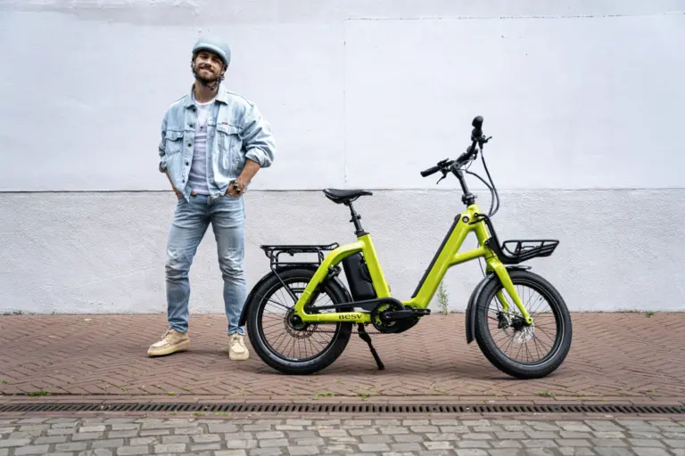 Limegrünes BESV CPT 1.0 E-Bike mit vorne montiertem Gepäckträger und hinterem Gepäckträger, daneben ein Mann mit Jeansjacke und Helm.