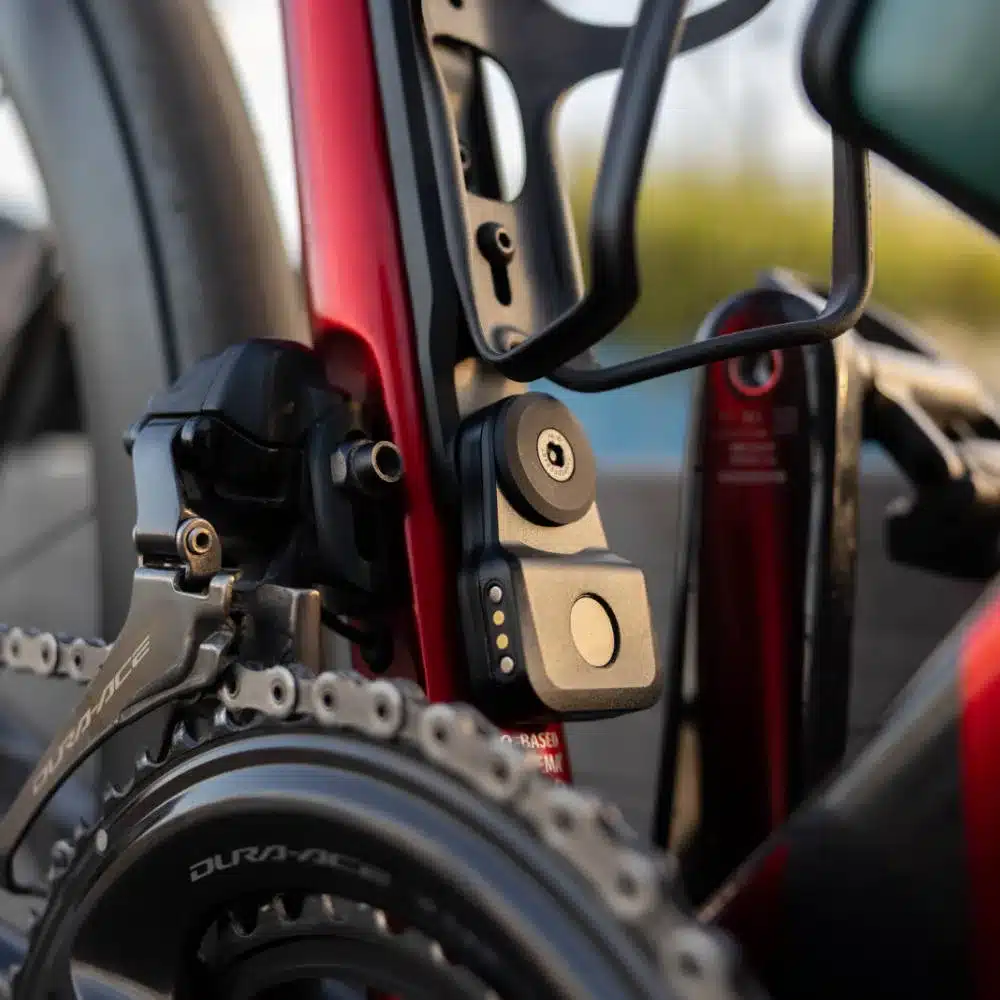 Nahaufnahme eines Quad Lock Alarm & Finder Geräts, montiert am Unterrohr eines roten Fahrradrahmens neben der Kette und dem Umwerfer.