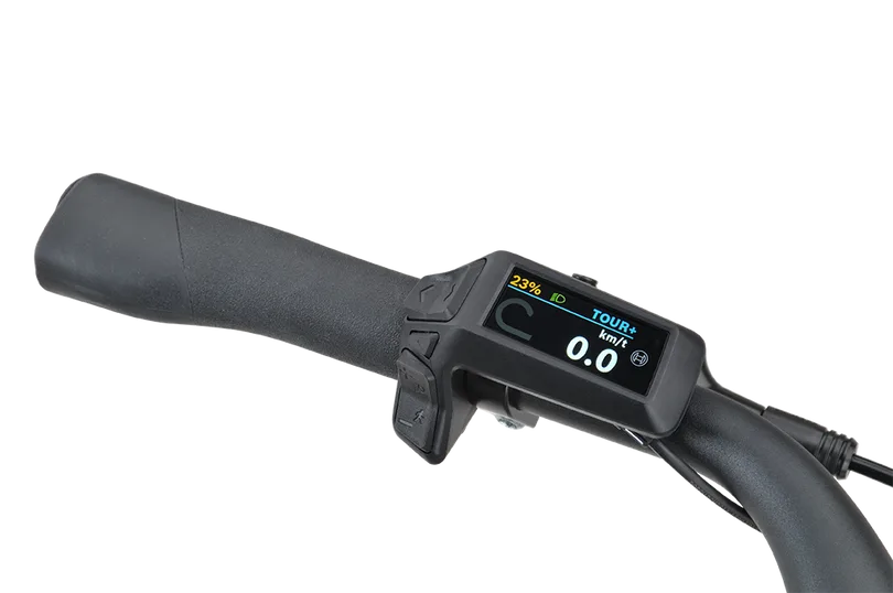 Nahaufnahme des Displays eines E-Bikes, das die Restreichweite von 23% und den Fahrmodus 'TOUR+' mit einer Geschwindigkeit von 0.0 km/h anzeigt, daneben ein schwarzer Lenkergriff.