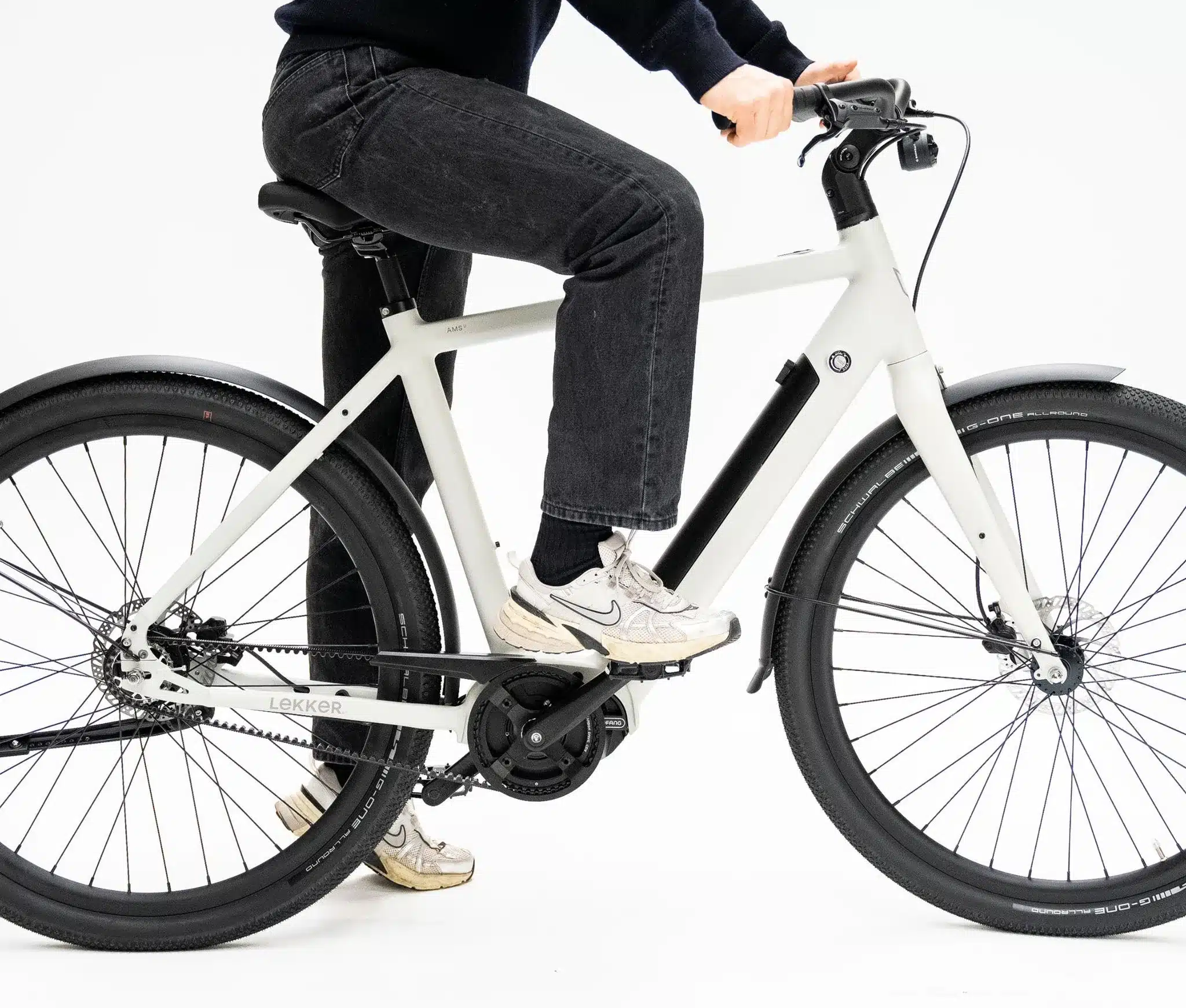 Person auf einem weißen Amsterdam Urban E-Bike, Fokus auf dem Gates CDX Riemenantrieb und der automatischen Schaltung.