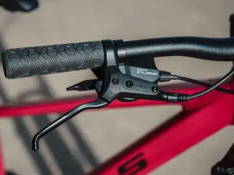 Nahaufnahme der linken Lenkerseite eines roten Kinderfahrrads der Marke BULLS. Zu sehen ist ein schwarzer Bremshebel, eine Shimano CUES Scheibenbremse und ein texturierter schwarzer Griff.