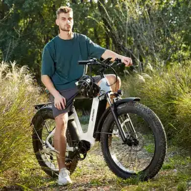 Ein Mann sitzt auf einem weißen HAOQI Eagle E-Bike mit dicken Reifen in einer natürlichen Umgebung.