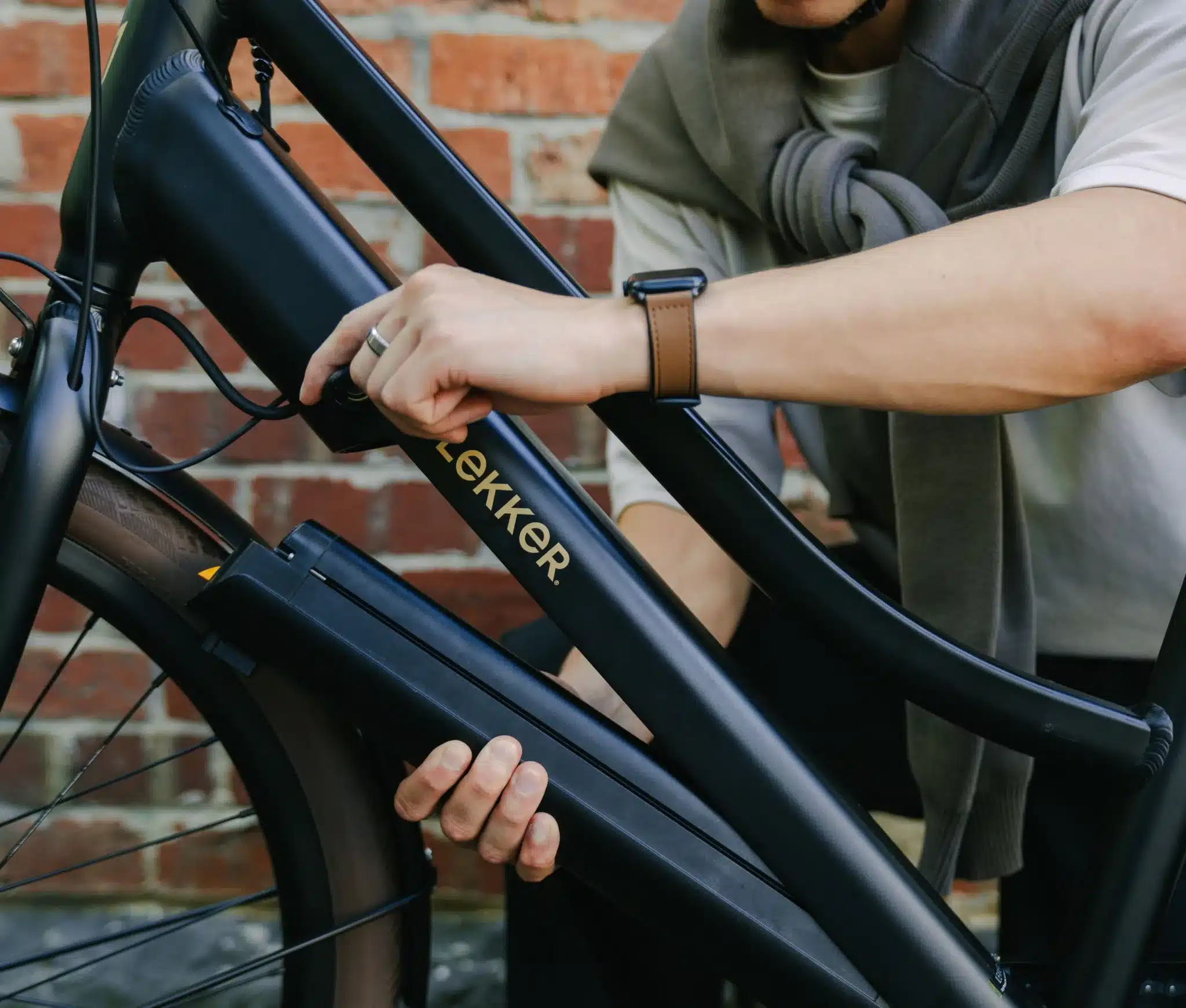 Nahaufnahme eines Mannes, der den Akku eines schwarzen LEKKER Jordaan Urban eBikes entnimmt. Auf dem Rahmen ist das LEKKER-Logo in Gold zu sehen.