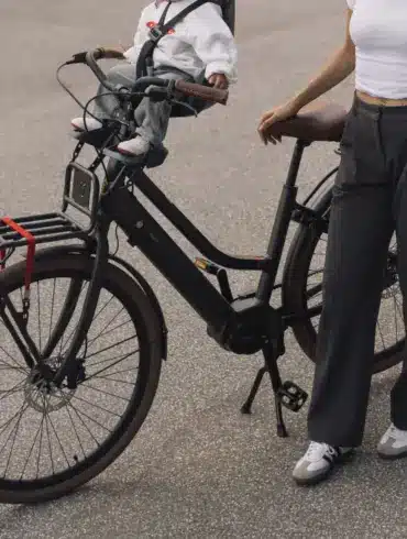 Ein schwarzes LEKKER Jordaan Urban eBike mit einem Kind im Front-Kindersitz. Eine Frau steht daneben.