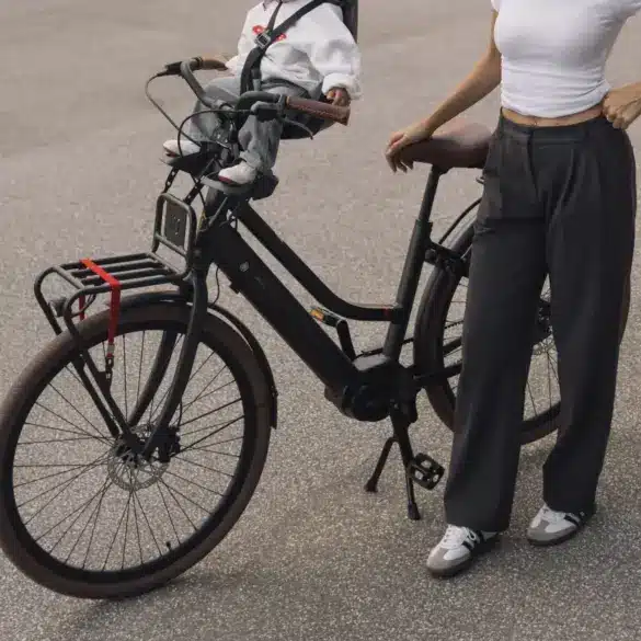 Ein schwarzes LEKKER Jordaan Urban eBike mit einem Kind im Front-Kindersitz. Eine Frau steht daneben.