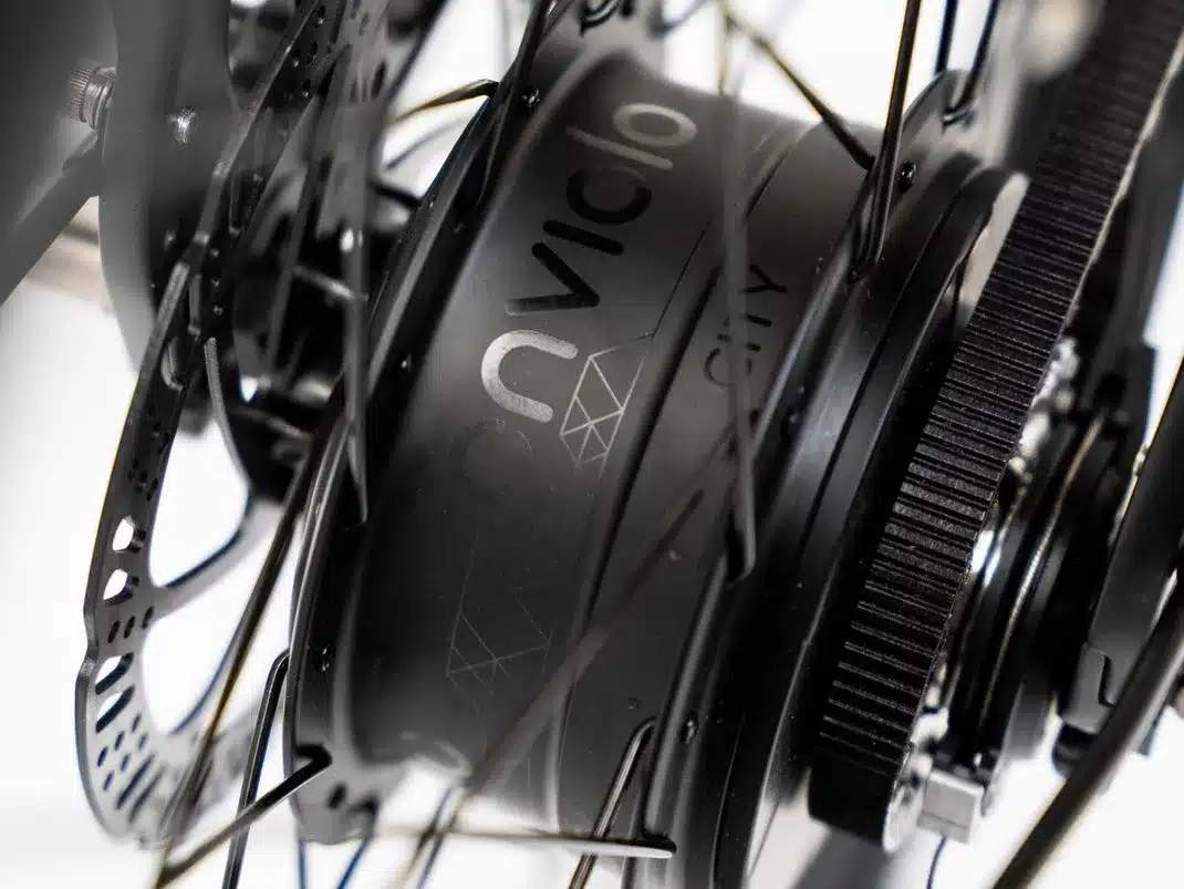 Detailbild der Enviolo CT Nabenschaltung und des Gates CDX Riemenantriebs an der Hinterradnabe eines schwarzen E-Bikes, wobei die Scheibenbremse sichtbar ist.