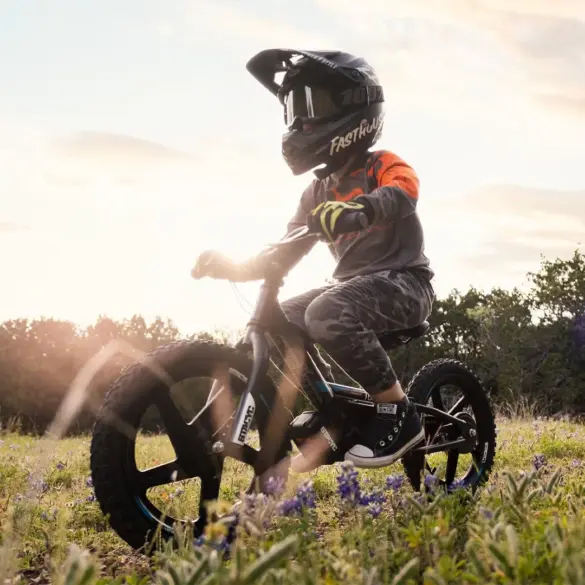 Kind mit Helm fährt elektrisches Laufrad STACYC 16eDRIVE BRUSHLESS auf einer blumenreichen Wiese.